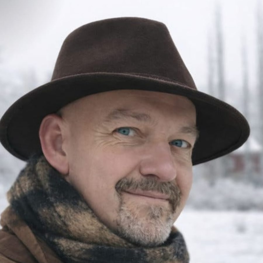 Marek Stark, sonriendo a la cámara, con sombrero y bufanda, en un paisaje nevado.
